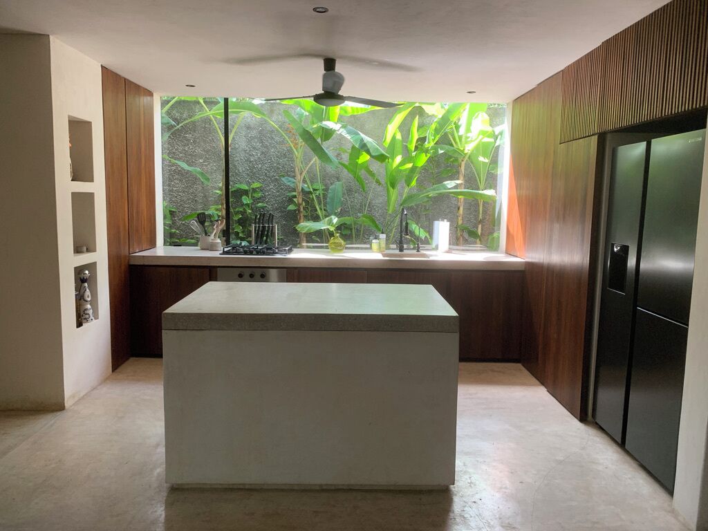 A modern kitchen with a central island, a window with a view of greenery, and a built-in refrigerator.