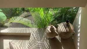 Ein kleiner, sonnendurchfluteter Bereich mit zwei Keramiktöpfen und einem Holztablett auf einem Balkon, umgeben von üppigem Grün.