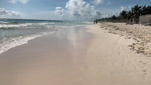 Ein weiter Sandstrand mit sanften Wellen, blauem Himmel und einigen Spaziergängern.