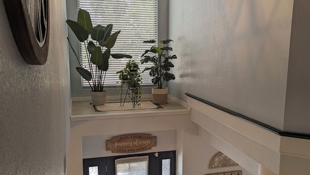 Een meerlaags interieur met een geometrisch plafondlicht, potplanten, een decoratief bord en een trap.