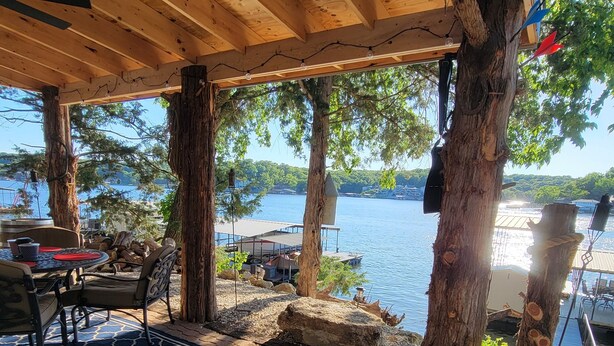 A covered outdoor seating area with a view of a lake, wooden furniture, and a dog. - Stay, Play, Getaway. Beautiful Lake Front Home-Large private dock  (Rocky Mount)