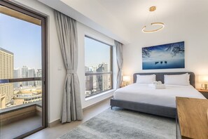 A hotel room with a large bed, a city view, a painting on the wall, and a modern light fixture.