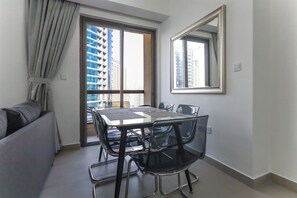 Uma sala de jantar moderna com mesa e cadeiras de vidro, um sofá e uma janela ampla com vista para edifícios altos.