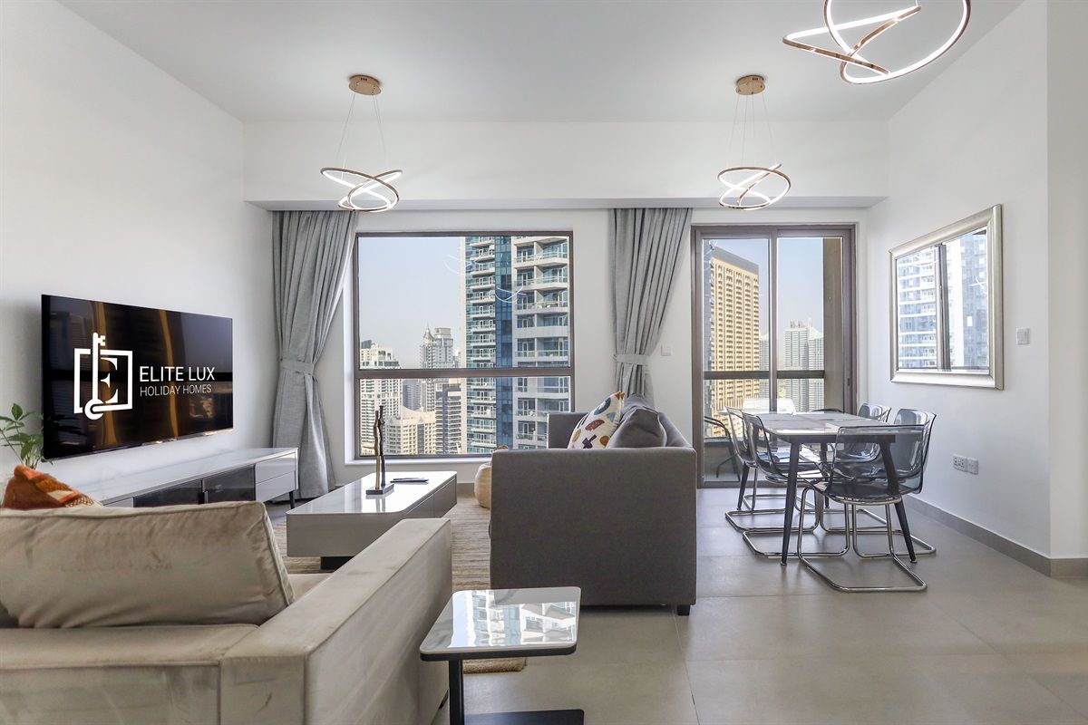Una sala moderna con una televisión de pantalla plana, un sofá, una mesa de comedor con sillas y ventanas amplias con vistas a la ciudad.