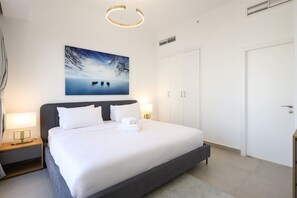 A modern bedroom with a large bed, a nightstand with a lamp, a wall-mounted artwork, and a door. - Beachside Haven Stylish 1 BHK in JBR Dubai (Dubai)