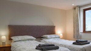 Ein Schlafzimmer mit zwei Betten, jeweils mit floralem Bettzeug, einem Nachttisch mit Lampe und einem Fenster mit gemusterten Vorhängen.