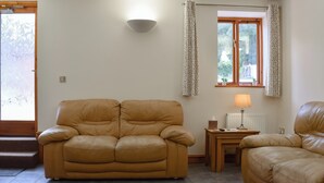 Ein Wohnzimmer mit zwei Ledersofas, einem kleinen Tisch mit einer Lampe und einem Fenster mit Vorhängen.