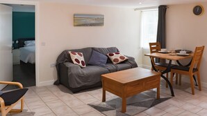 Ein modernes Wohnzimmer mit grauem Sofa, Couchtisch aus Holz und Essbereich mit Stühlen und Tisch für zwei Personen.