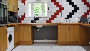 Eine moderne Küche mit Holzausstattung, einer integrierten Waschmaschine, einer Mikrowelle und einem Spülbecken mit Fenster darüber.