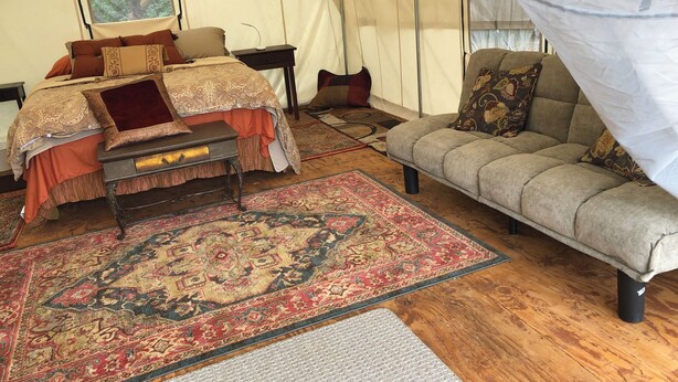Une pièce aménagée comme une tente, avec un lit, un canapé, un tapis et un lit à baldaquin.