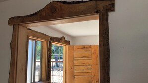 Un cadre de porte en bois avec une fenêtre, une porte en bois, et une vue sur un espace extérieur doté d’une rambarde et d’arbres.