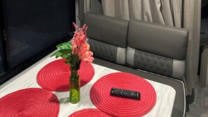 A compact living space with a television mounted on the wall, a sofa, a small table with a remote control, and a decorative vase with flowers. - “NATURE IN THE CITY” (Orlando)
