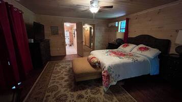 Een slaapkamer met een houten plafond, een bed met bloemenbedrukking, een nachtkastje, een dressoir en een rood gordijn.