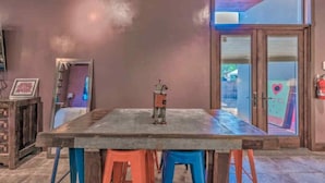 A dining area with a large table and colorful stools, a small heater, and a view through a glass door. - Colorful & Unique Ruidoso Studio Escape in Midtown (Ruidoso)