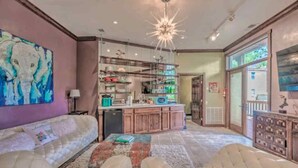 A spacious living area with a sofa, ottomans, a kitchen with a bar, and a large painting on the wall. - Colorful & Unique Ruidoso Studio Escape in Midtown (Ruidoso)