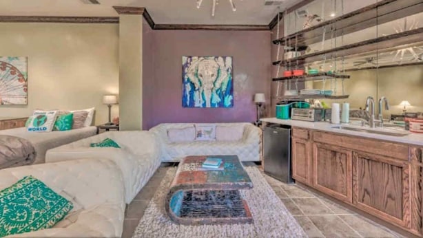 A modern living room with a sofa, a coffee table, and a kitchen area with wooden cabinets and a sink. - Colorful & Unique Ruidoso Studio Escape in Midtown (Ruidoso)