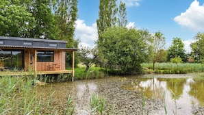 A wooden cabin with a deck overlooking a pond surrounded by lush greenery. - 1 bedroom accommodation in Boys Hill, near Sherborne (Boys Hill, near Sherborne)