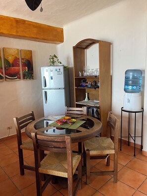 Cozy kitchen area with a round dining table and four chairs, featuring a refrigerator, water dispenser, and ample storage.