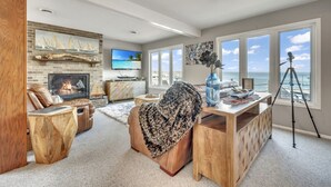 Amplia sala de estar con chimenea, muebles de cuero, un televisor grande y vista al océano a través de amplias ventanas.