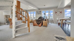A spacious living area with a staircase, a fireplace, a dining area, and large windows offering a view.