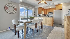 Una cocina moderna con armarios de madera, un refrigerador de acero inoxidable y un comedor con mesa y sillas de vidrio.