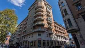 A multi-story building with balconies, a ground-level shop, and parked cars. - Sulla via del treno by Wonderful Italy (Turin)