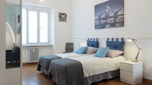 A bedroom with two beds, a window, a radiator, a desk, and a chair. - Sulla via del treno by Wonderful Italy (Turin)