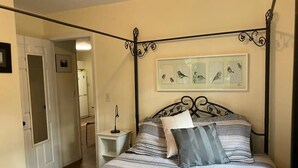 A bedroom with a four-poster bed, striped bedding, a bedside table with a lamp, and a framed bird artwork on the wall. - The Lazy Susan (Charleston)