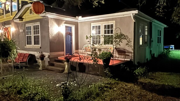 A two-story house with a red door, a porch with a bench, and a small garden area. - The Lazy Susan (Charleston)