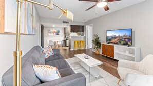 A modern living room with a gray sofa, a white coffee table, and a ceiling fan. - Soco 2BR Corner Suite w Pool King bed Fast Wifi (Austin)
