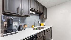 A modern kitchen with dark wooden cabinets, a white countertop, a built-in dishwasher, and a coffee maker. - Soco 2BR Corner Suite w Pool King bed Fast Wifi (Austin)