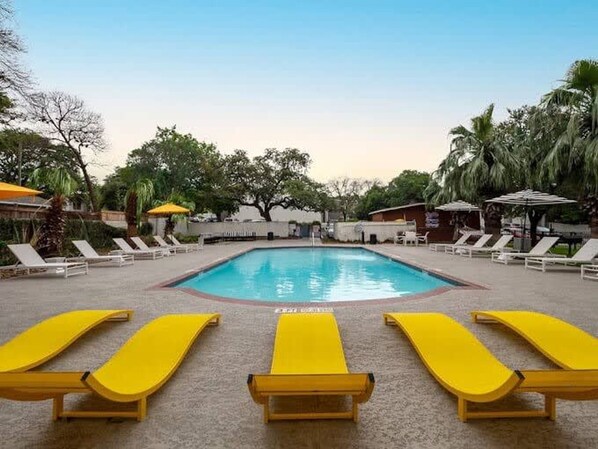 A swimming pool with sun loungers and umbrellas, surrounded by trees and a clear sky. - Soco 2BR Corner Suite w Pool King bed Fast Wifi (Austin)