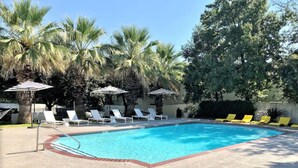 A swimming pool with lounge chairs and umbrellas, surrounded by palm trees. - Soco 2BR Corner Suite w Pool King bed Fast Wifi (Austin)