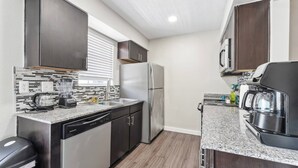 Una cocina compacta con muebles oscuros, un refrigerador de acero inoxidable, un microondas integrado y una cafetera.