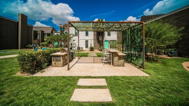 Patio trasero con cerramiento de vidrio, zona de barbacoa y sendero de piedra que conduce a una casa.