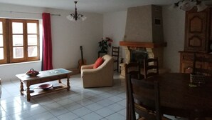 A living room with a fireplace, a dining table, a sofa, and a guitar. - HOUSE 8-9 people LAVAUDIEU, most beautiful village in France. Pets allowed. (Lavadieu)
