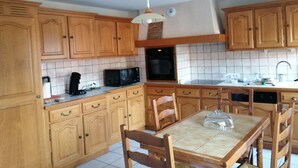 A kitchen with wooden cabinets, a microwave, an oven, and a dining table with chairs. - HOUSE 8-9 people LAVAUDIEU, most beautiful village in France. Pets allowed. (Lavadieu)