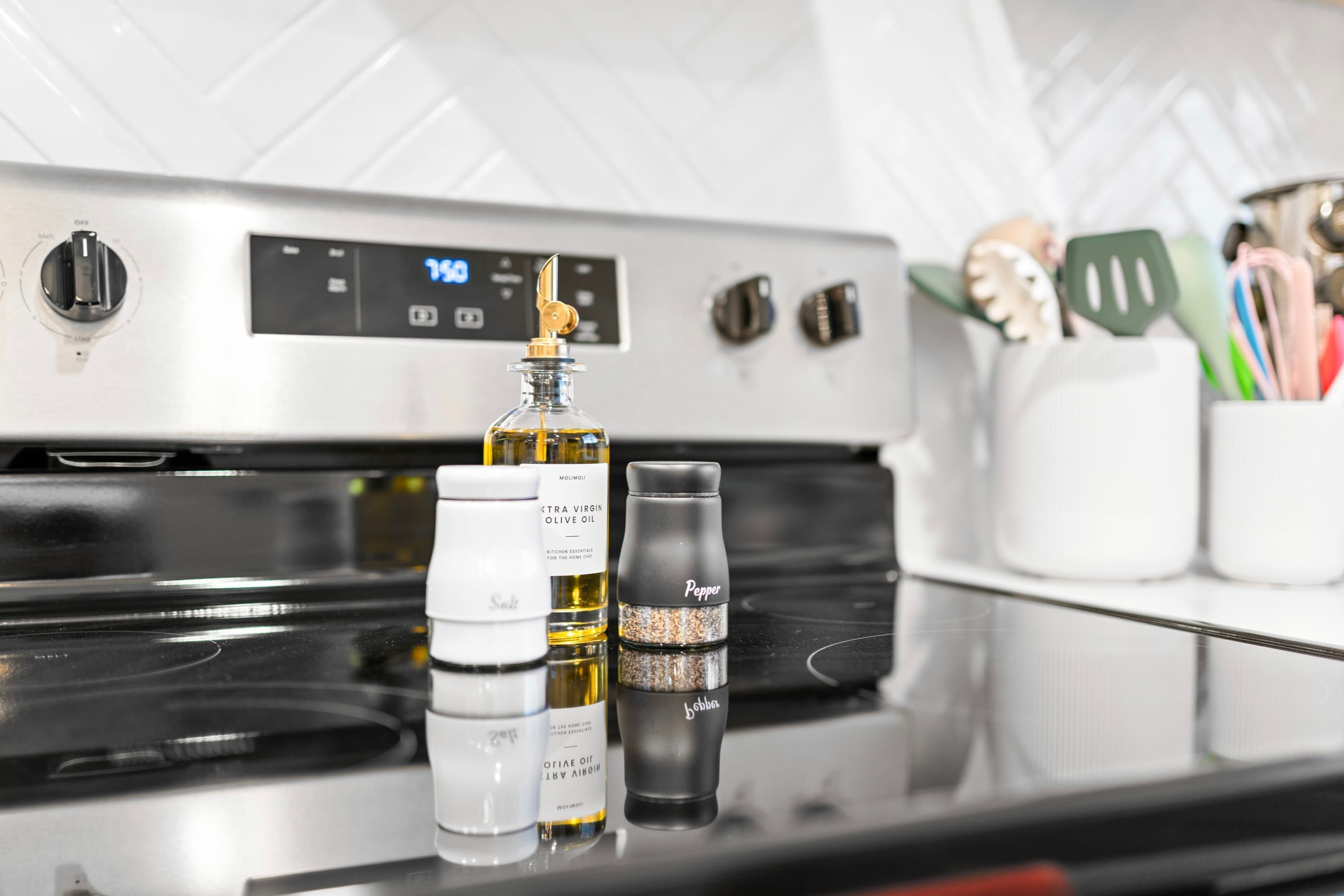 A kitchen with a stainless steel stove, a digital clock, and various kitchen items like bottles and utensils.