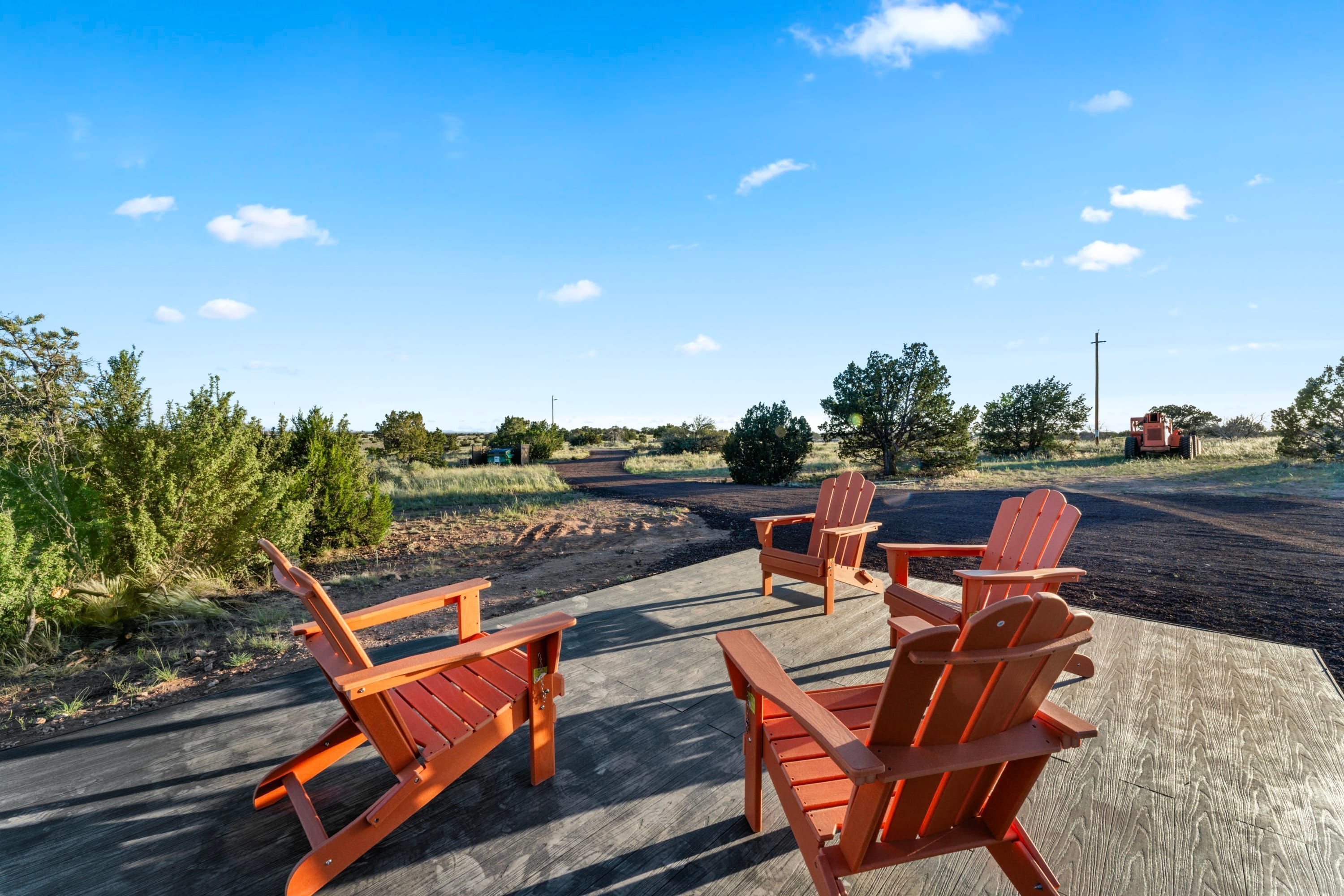 A deck with wooden chairs and a table, surrounded by greenery and a clear sky.