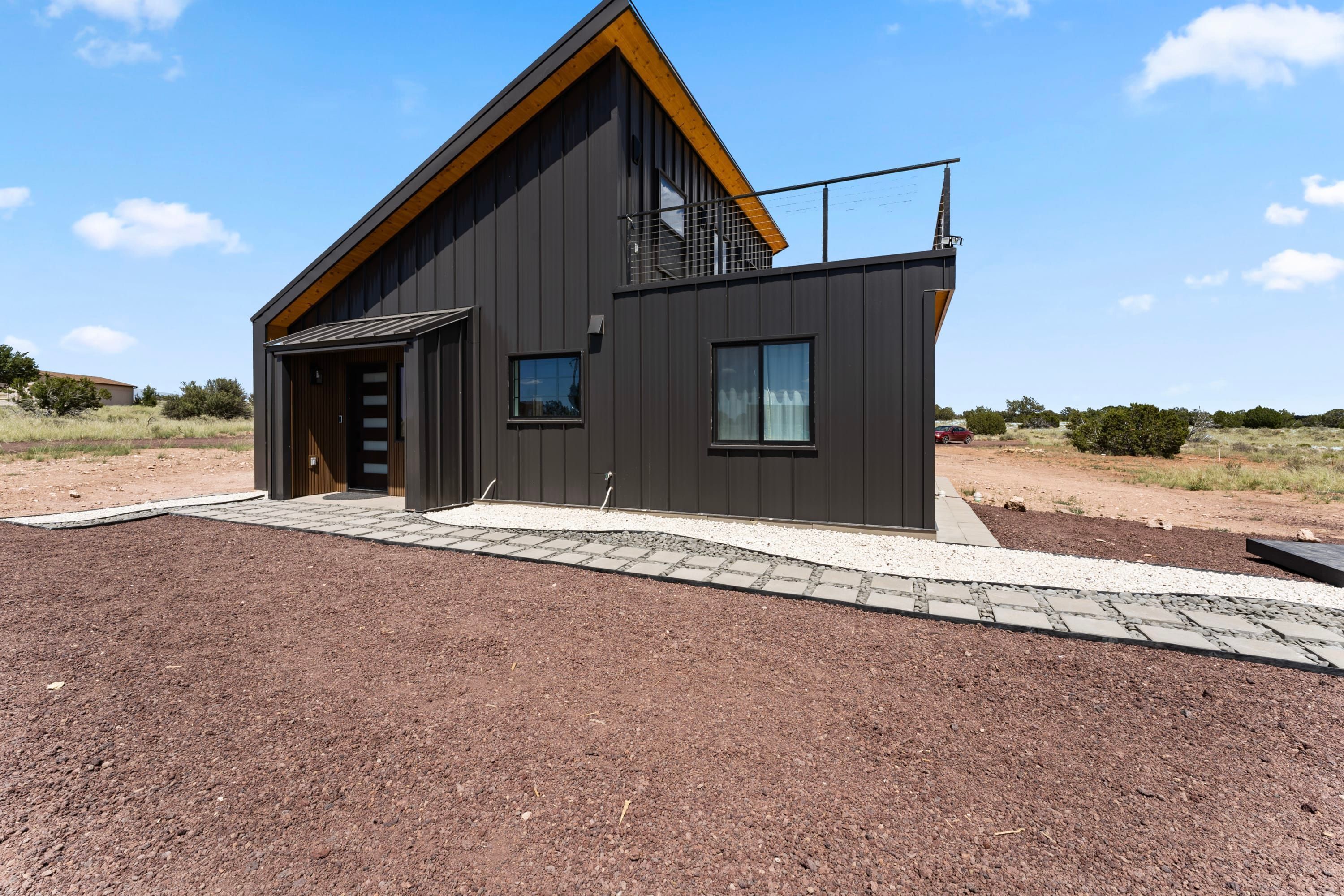 A modern two-story house with a dark exterior, a wooden roof, and a small balcony.