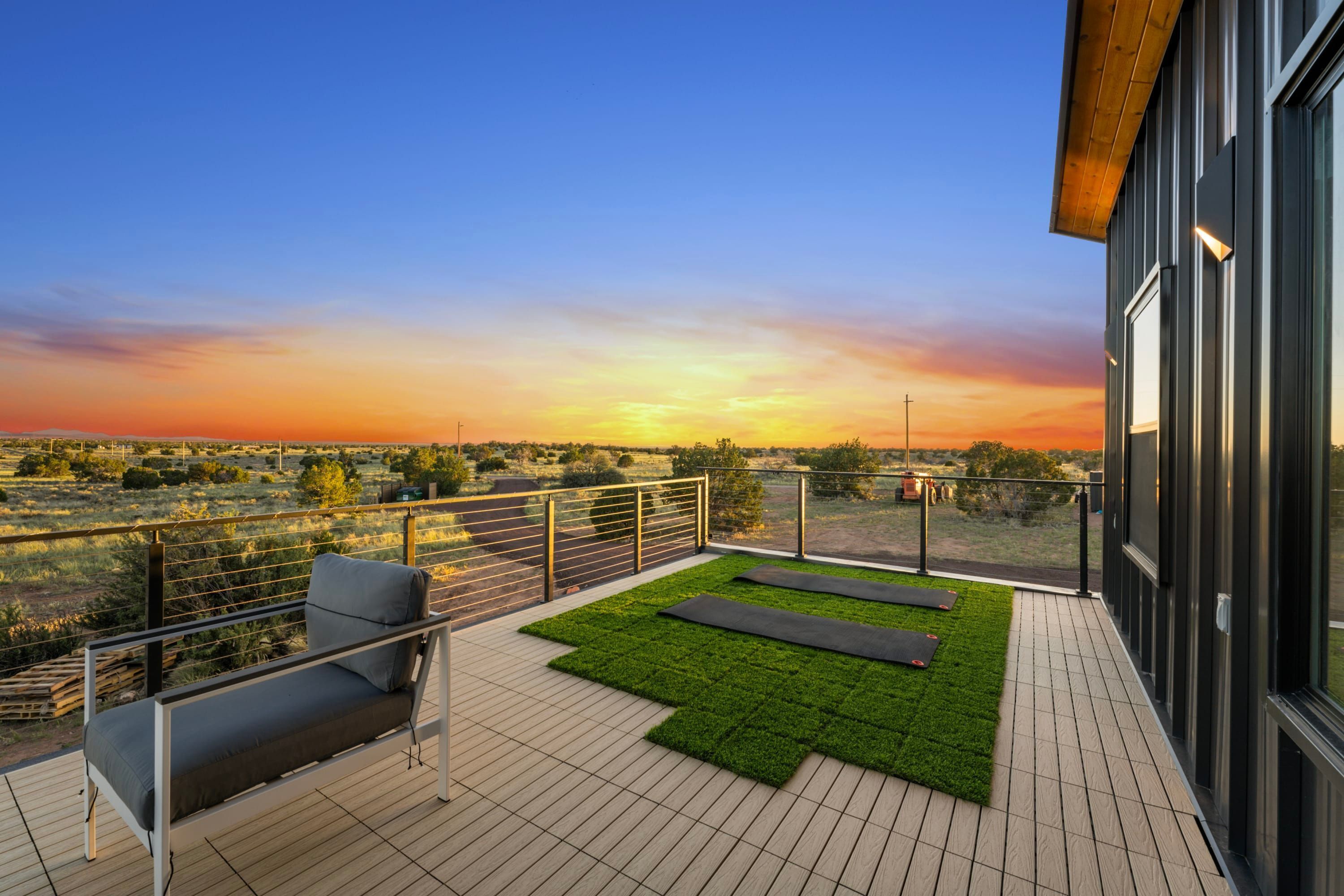 Een balkon met uitzicht op de ondergaande zon, een comfortabele bank en een stukje kunstgras.