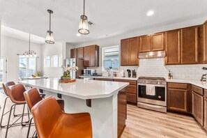 A modern kitchen with a large island, stainless steel appliances, and wooden cabinets.