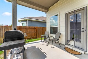 Eine überdachte Terrasse mit Grill, Tisch und Stühlen.