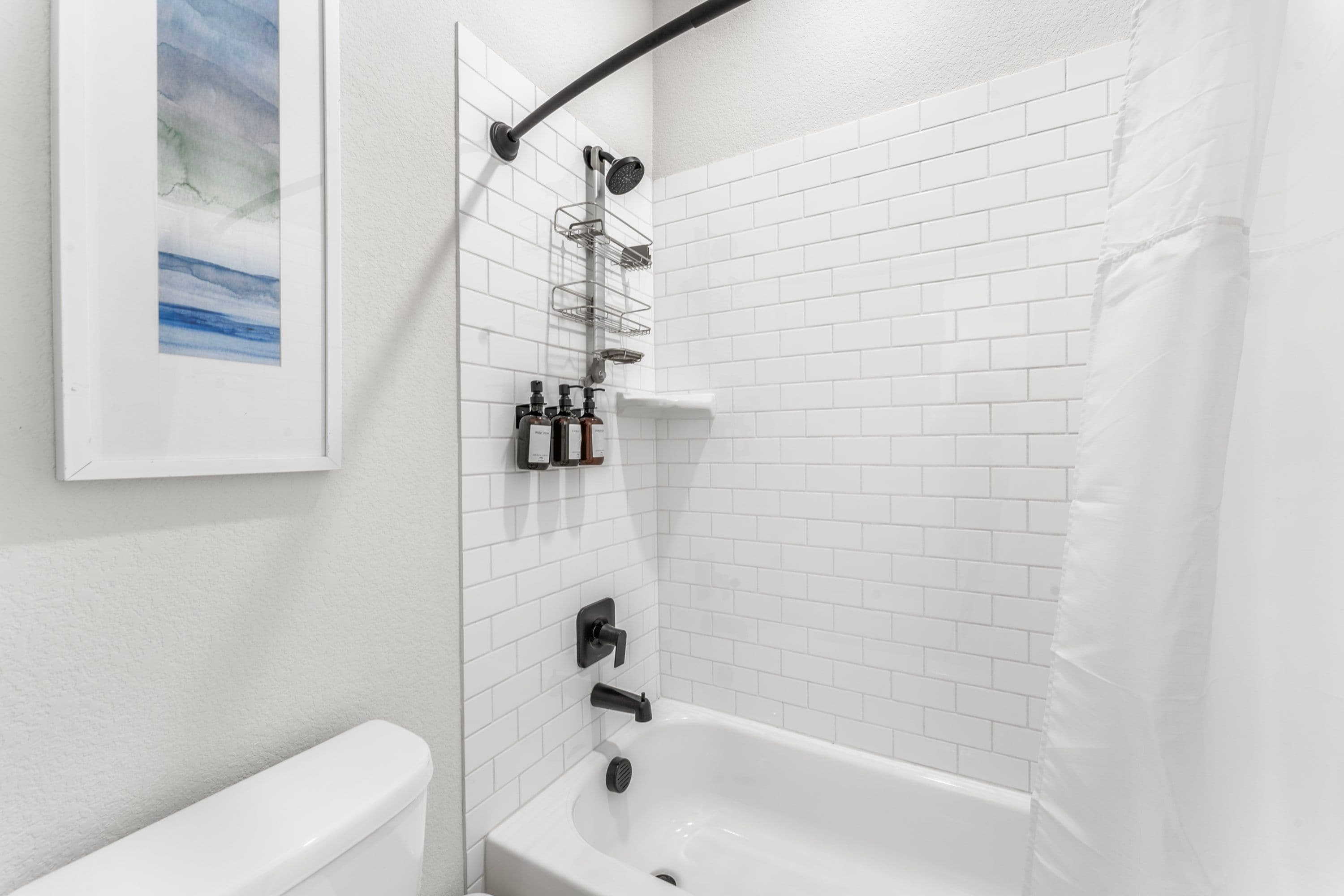 A modern bathroom with white subway tiles, a white bathtub, a shower with a black hose, and a wall-mounted soap dispenser.