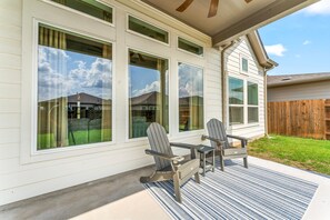 A house with large windows, a porch with two Adirondack chairs, and a wooden fence in the background.