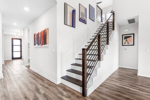 A modern interior with a wooden staircase, white walls, and a hallway leading to a door.