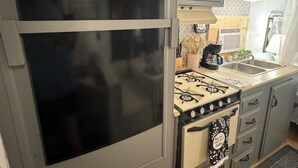 Een kleine keuken met een kookplaat, gootsteen en een groot raam.