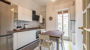 A modern kitchen with white cabinetry, stainless steel appliances, and a wooden dining table with white chairs.