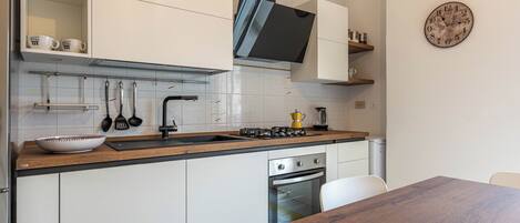 Una cocina moderna con armarios blancos, encimera de madera y horno empotrado.