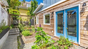 A wooden house with a blue door and windows, a garden with various plants, and a pathway leading to the entrance. - Charming Urban Cottage in Cap Hill (Seattle)